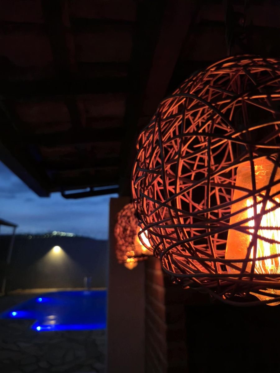 Luminárias de palha acesas na área gourmet com a piscina azul ao fundo