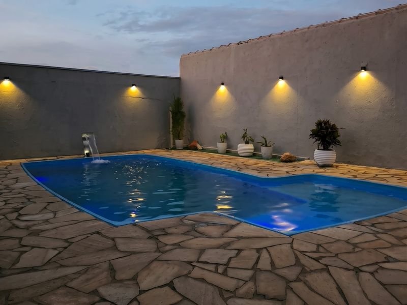 Piscina com luz azul e arandelas acesas no muro, projeto Domus em Sete Lagoas